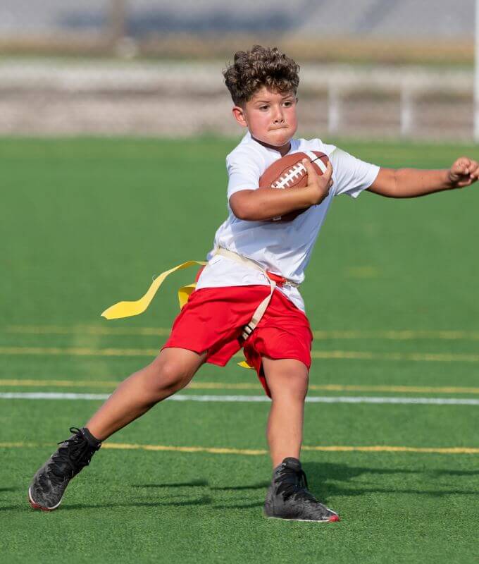 Boy running in turf field while holding football