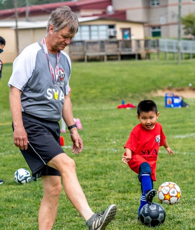 Volunteer coach showing a little boy how to kick a ball